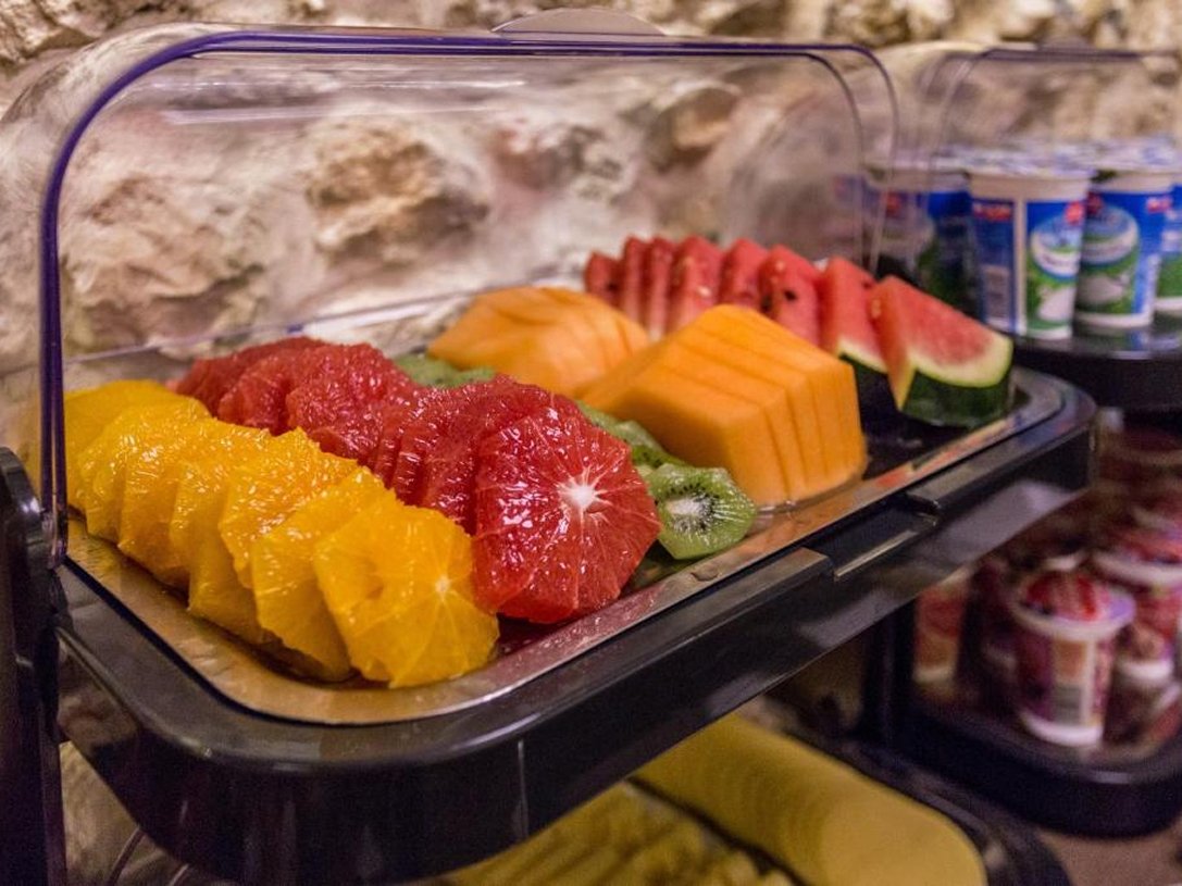 Pokrojone plasterki pomarańczy, czerwonych grejpfrutów, kiwi, melona i arbuzów na tacy pod przezroczystą przykrywką.