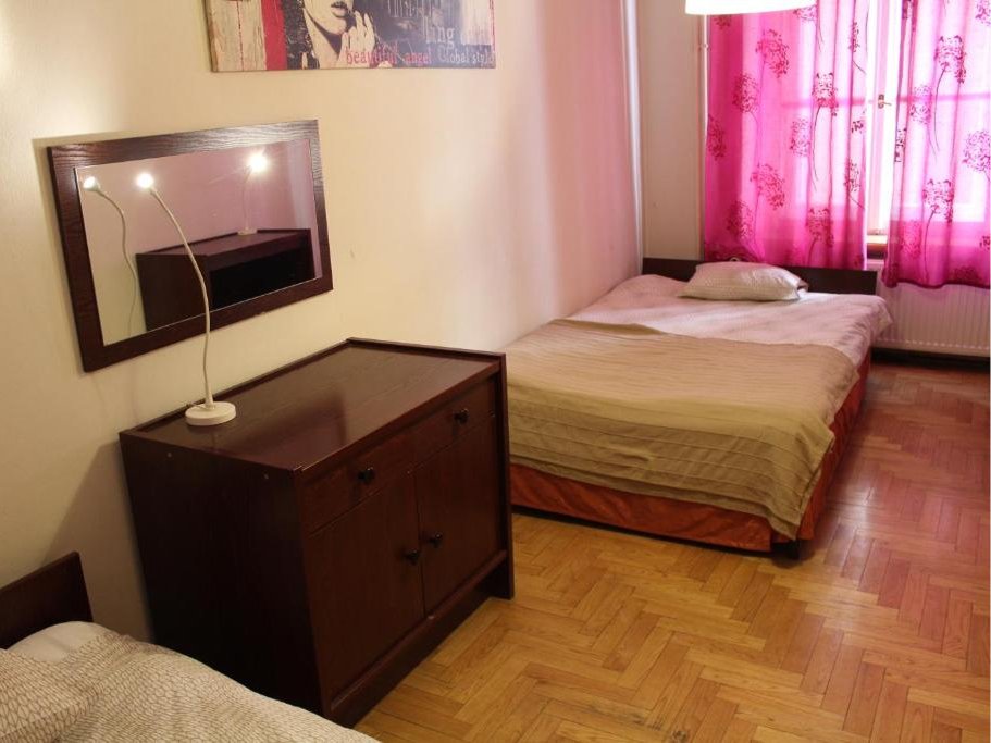 Pokój z podwójnym łóżkiem po lewej stronie oraz dwoma pojedynczymi łóżkami po prawej stronie, dekorowane tapetą i zasłonami.