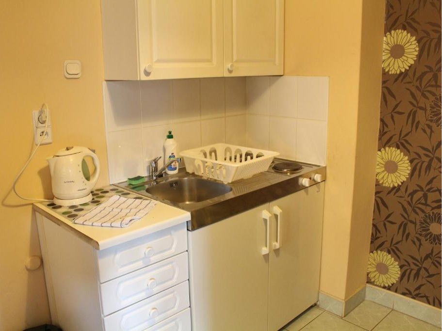 Pokój z łóżkiem przykrytym białą pościelą i szarą narzutą, biurkiem z dwoma krzesłami oraz telewizorem zamontowanym na ścianie.